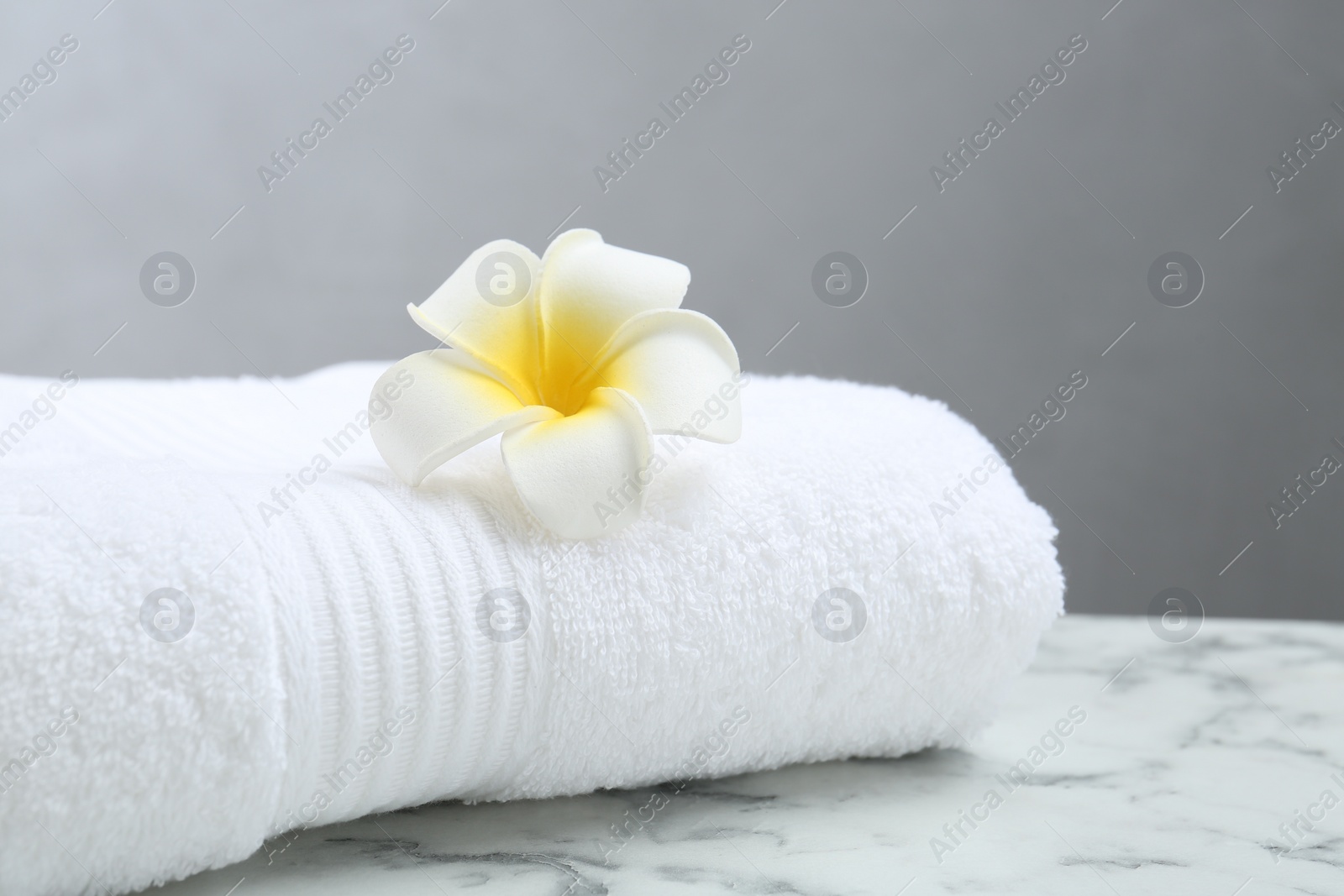Photo of Folded terry towel and plumeria flower on white marble table, closeup. Space for text