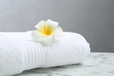 Folded terry towel and plumeria flower on white marble table, closeup. Space for text