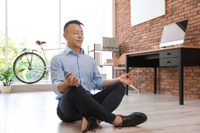 Photo of Young businessman doing yoga exercises in office. Workplace fitness