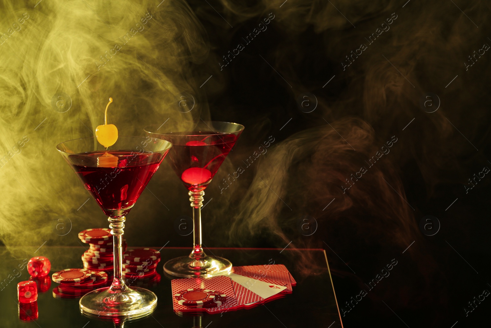 Photo of Casino chips, dice, playing cards and cocktails on dark background with smoke, space for text