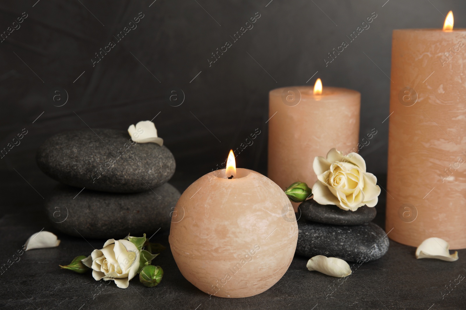 Photo of Burning candles, spa stones and flowers on dark grey table