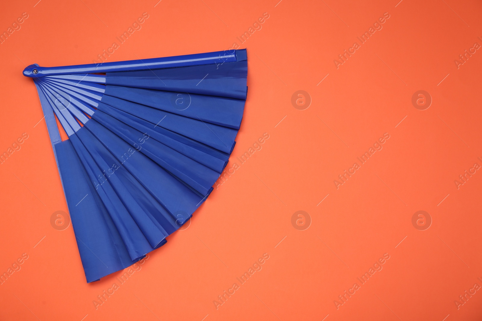 Photo of Bright blue hand fan on orange background, top view. Space for text