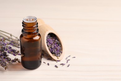 Photo of Bottle of essential oil and lavender flowers on white wooden table, space for text