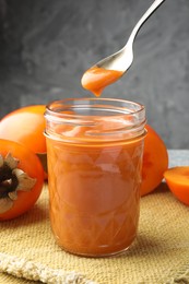 Photo of Taking delicious persimmon jam with spoon from glass jar on table