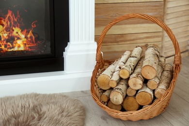 Photo of Firewood in wicker basket near burning fireplace indoors