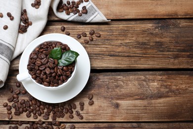 Photo of Cup with roasted coffee beans and leaves on wooden table, flat lay. Space for text