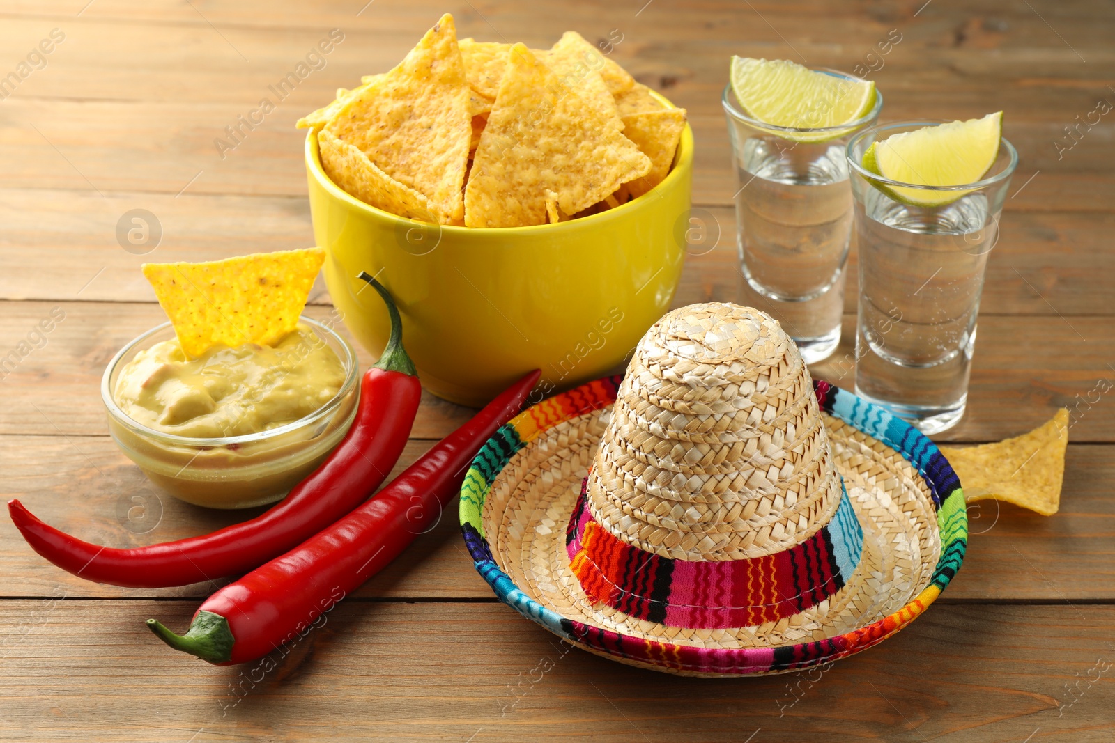 Photo of Mexican sombrero hat, tequila, chili peppers, nachos chips and guacamole on wooden table