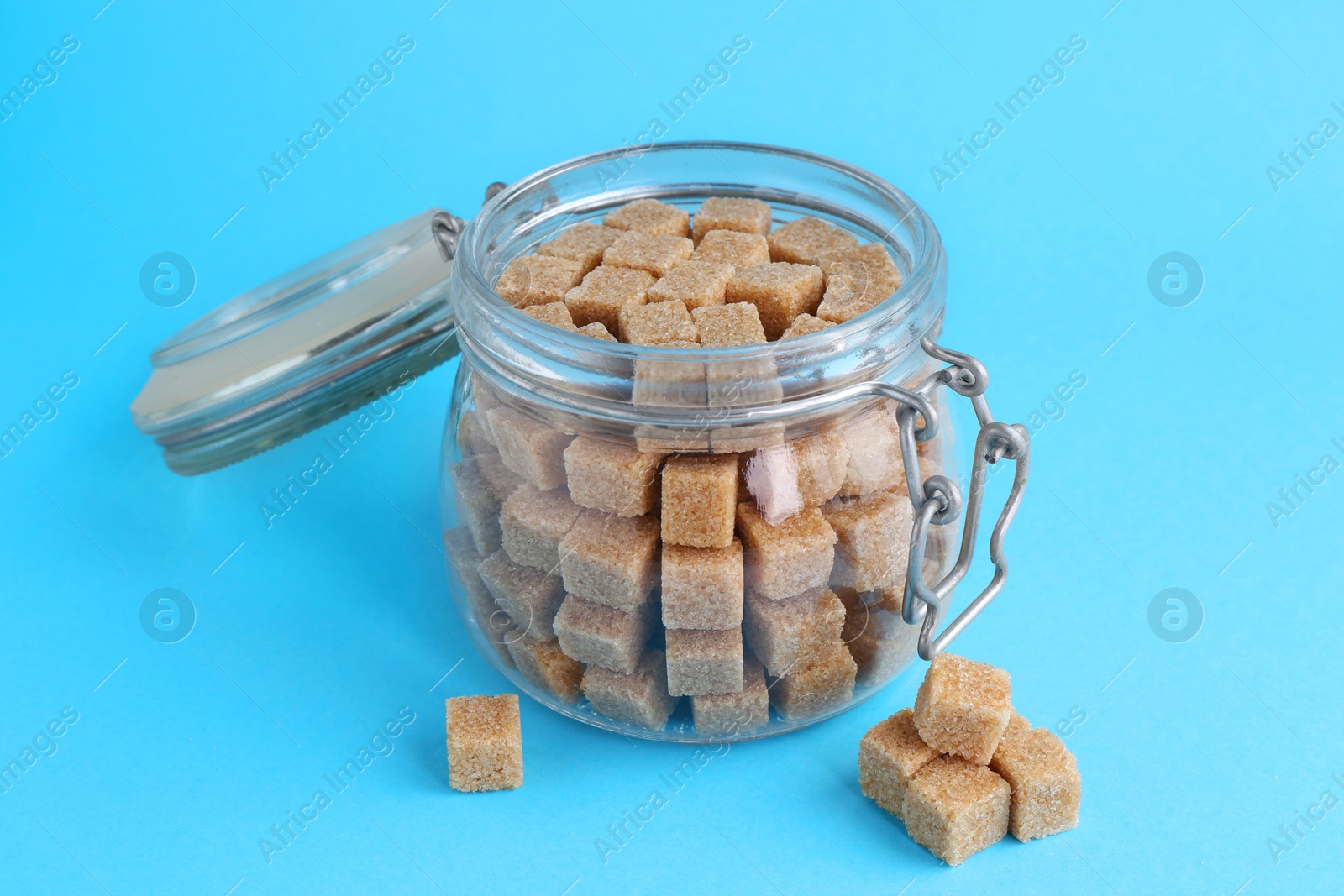 Photo of Brown sugar cubes in glass jar on light blue background