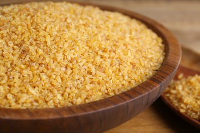 Photo of Bowl with uncooked bulgur on wooden table, closeup