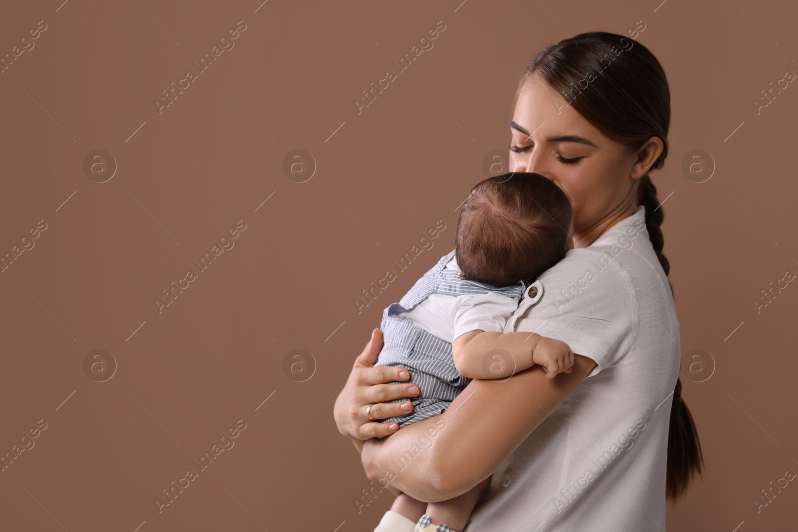 Photo of Mother holding her cute newborn baby on brown background, space for text