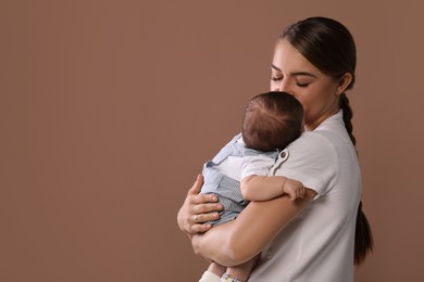 Mother holding her cute newborn baby on brown background, space for text
