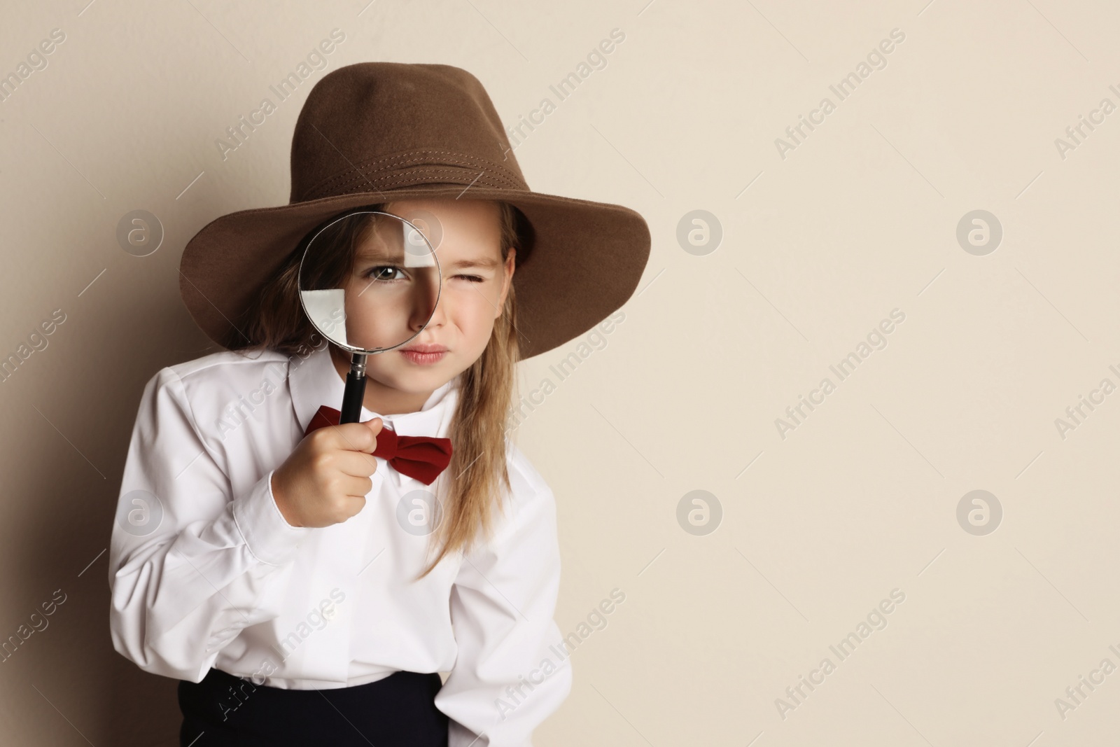 Photo of Cute little child in hat with magnifying glass playing detective on beige background, space for text