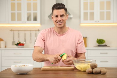 Photo of Man peeling potato at table in kitchen. Preparing vegetable