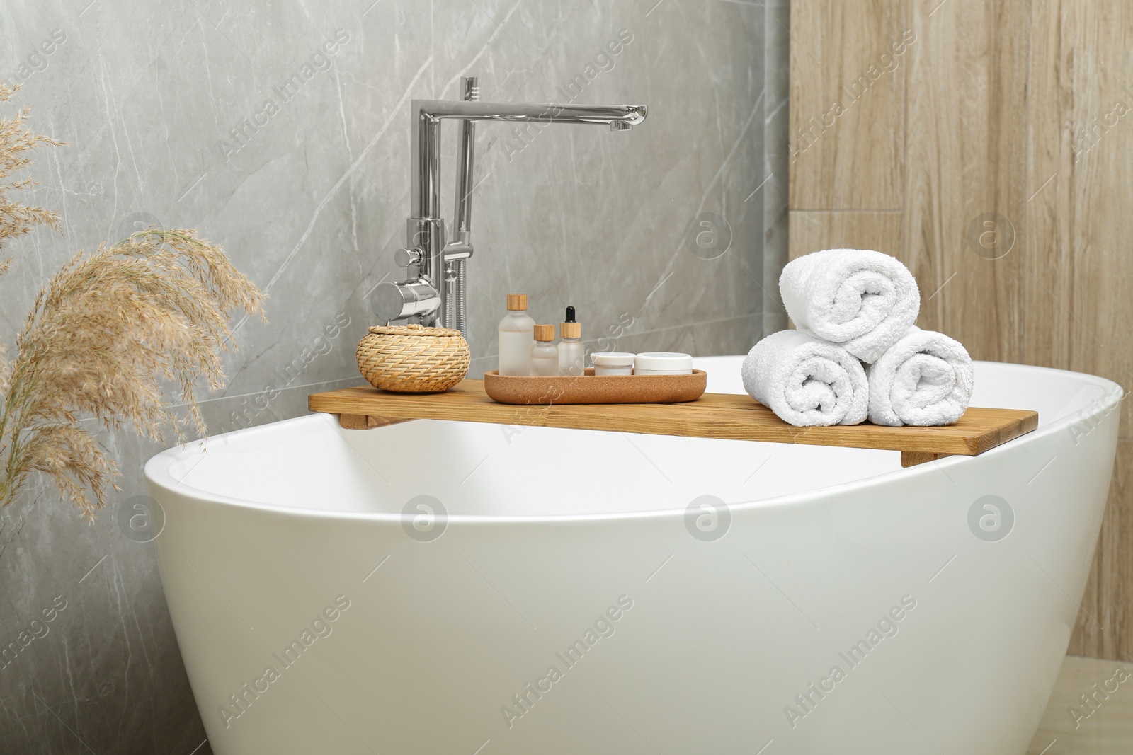 Photo of Rolled bath towels and personal care products on tub tray in bathroom