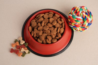 Vitamins, toy and dry pet food in bowl on beige background, above view