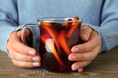 Photo of Woman holding glass cup of tasty mulled wine at wooden table, closeup