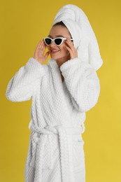 Beautiful young woman in bathrobe and sunglasses on yellow background