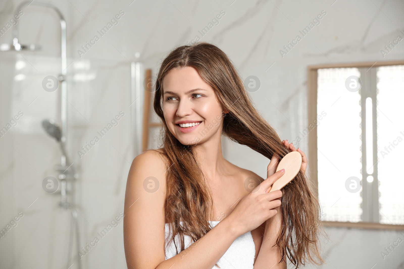 Image of Beautiful young woman brushing wet hair in bathroom
