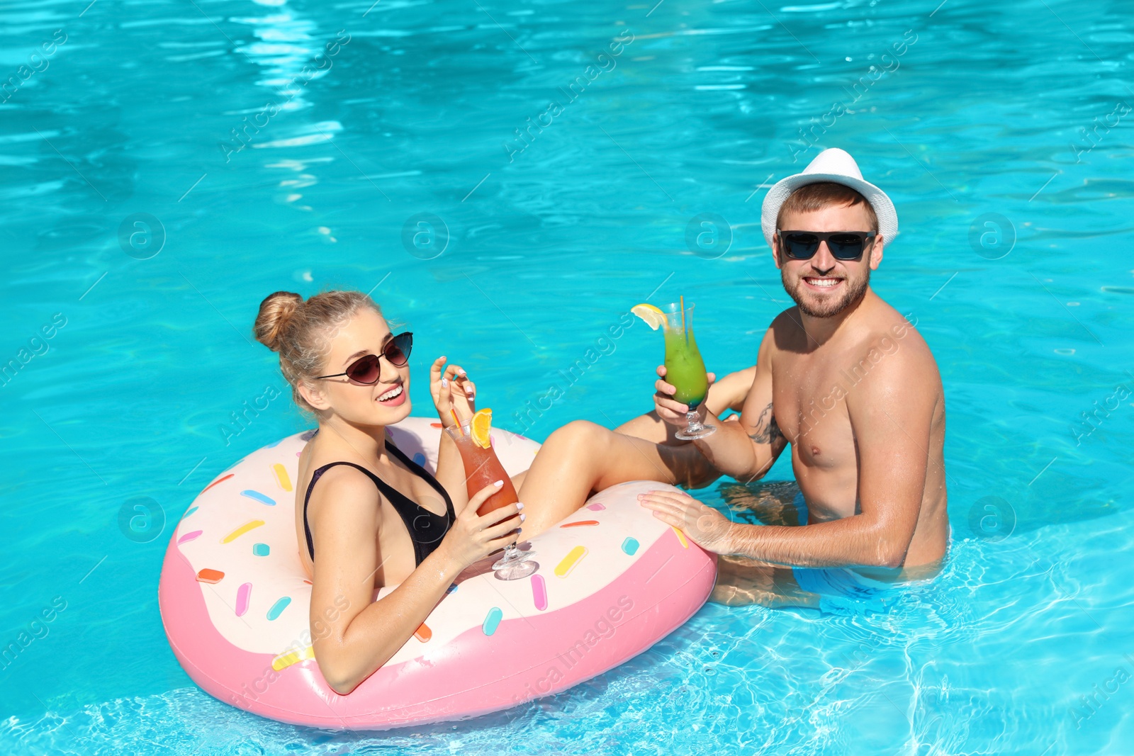 Photo of Young couple with refreshing cocktails and inflatable ring in swimming pool