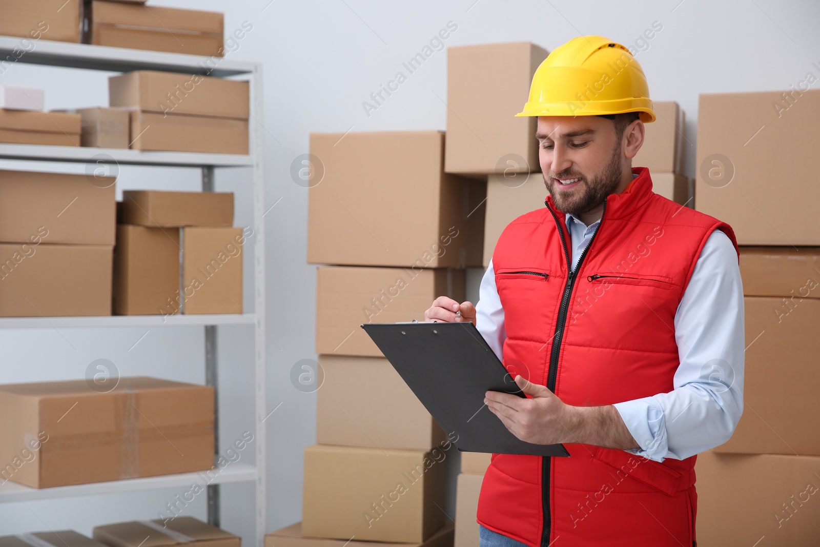 Photo of Young man with clipboard near cardboard boxes at warehouse