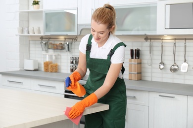 Photo of Female janitor cleaning table with rag in kitchen