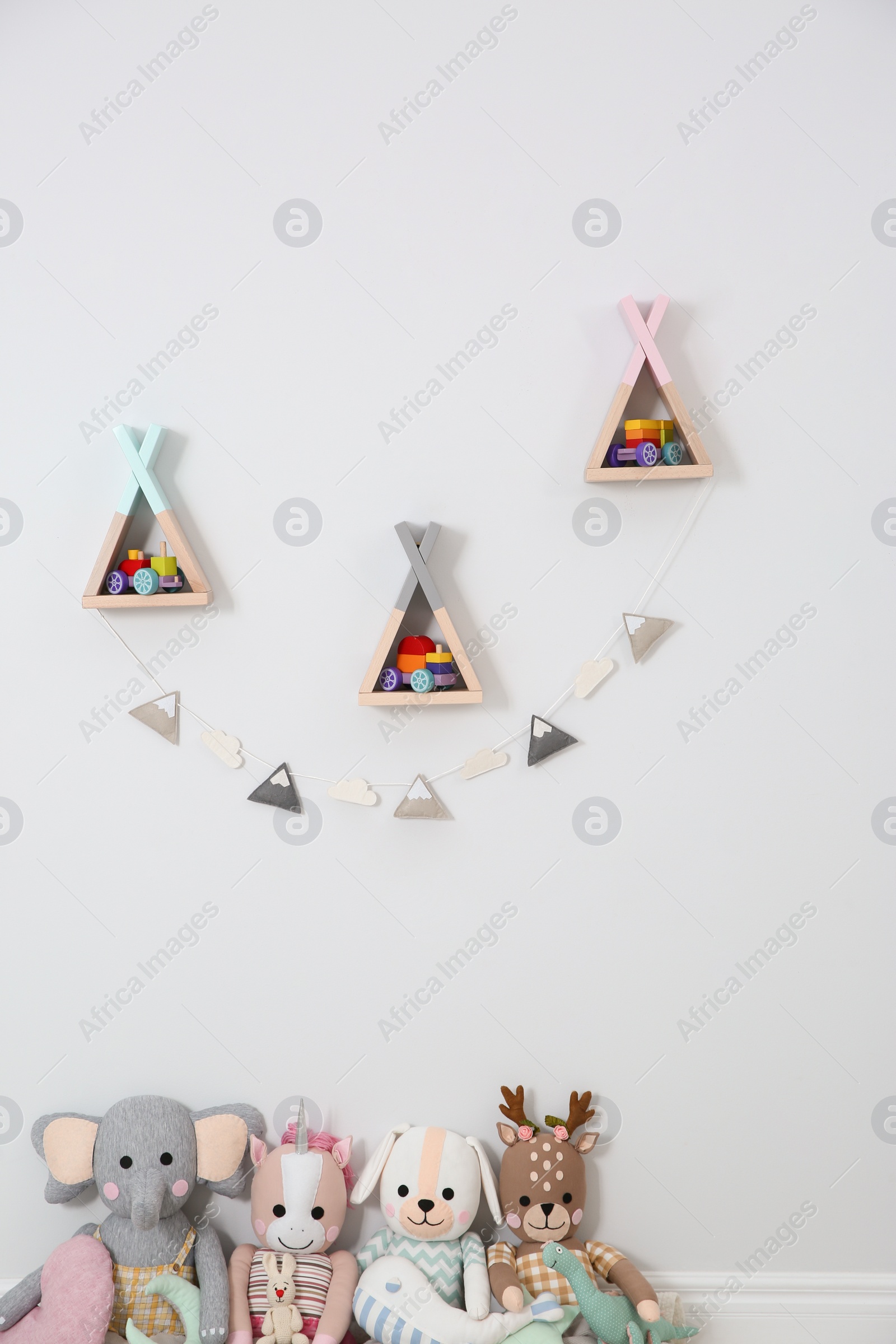 Photo of Wigwam shaped shelves, stuffed toys and garland indoors. Children's room interior design