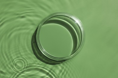 Photo of Stylish presentation for product. Glass podium in water on pale green background, top view