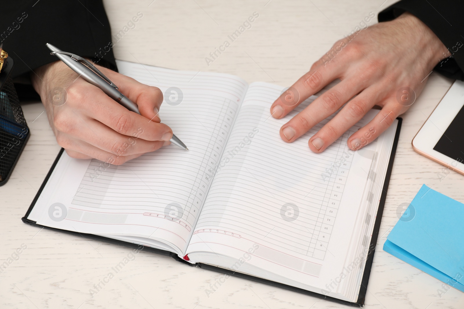 Photo of Man taking notes at white wooden table, closeup