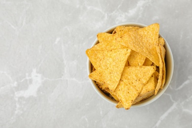 Photo of Bowl with tasty Mexican nachos chips on grey table, top view. Space for text