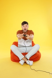 Emotional man playing video games with controller on color background