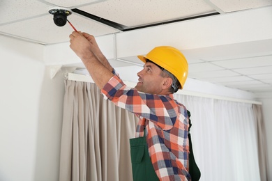Photo of Electrician with screwdriver repairing CCTV camera indoors
