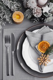 Photo of Festive place setting with beautiful dishware, fabric napkin and dried orange slice for Christmas dinner on grey table, flat lay
