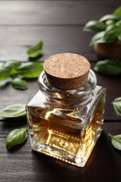 Glass bottle of basil essential oil and leaves on wooden table