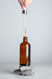 Photo of Woman dripping hydrophilic oil into bottle at white table, closeup