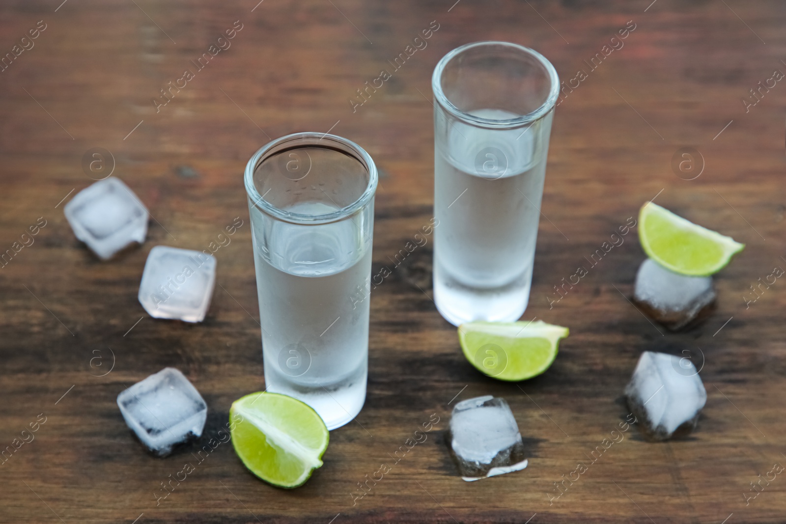 Photo of Mexican tequila shots with lime slices and ice cubes on wooden table. Drink made from agave