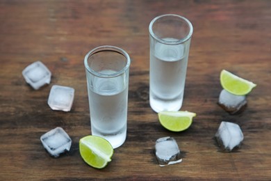 Photo of Mexican tequila shots with lime slices and ice cubes on wooden table. Drink made from agave