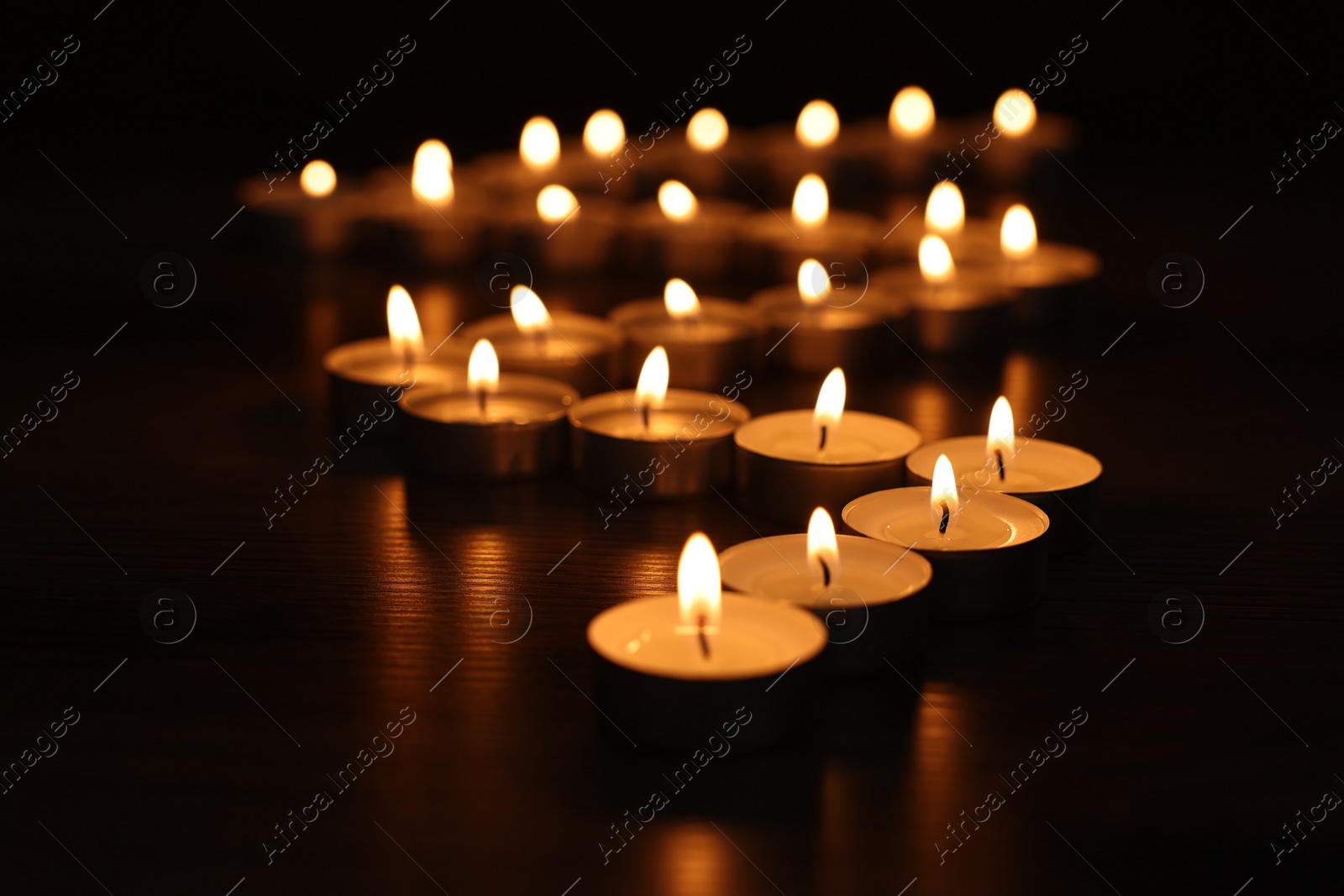 Photo of Burning tealight candles on dark surface, closeup