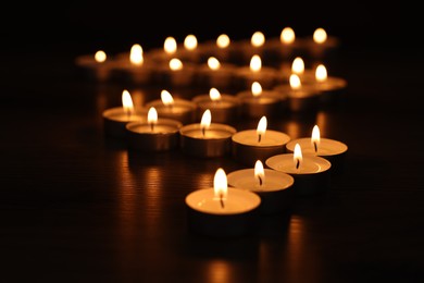 Photo of Burning tealight candles on dark surface, closeup