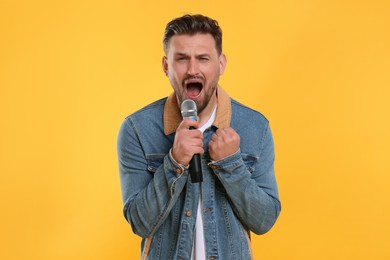 Handsome man with microphone singing on yellow background