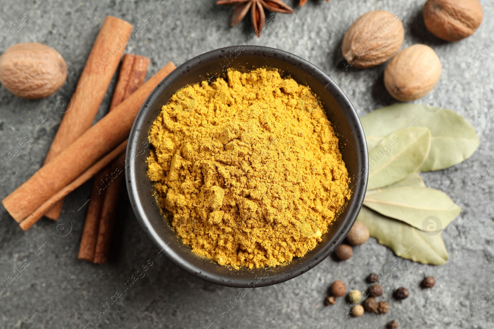 Photo of Dry curry powder in bowl and other spices on dark textured table, flat lay