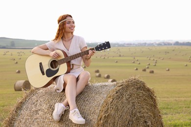 Photo of Beautiful hippie woman playing guitar on hay bale in field, space for text