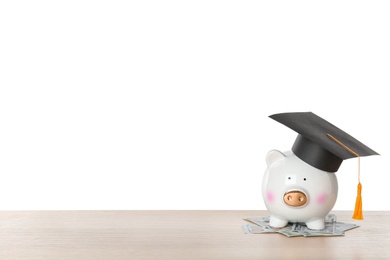 Piggy bank with graduation hat and money on table against white background