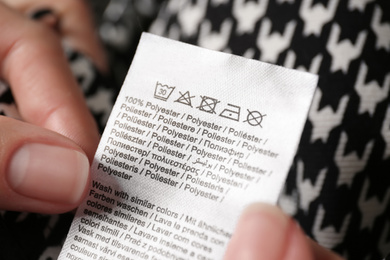 Photo of Woman reading clothing label with care symbols and material content on shirt, closeup