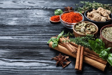Different natural spices and herbs on black wooden table. Space for text
