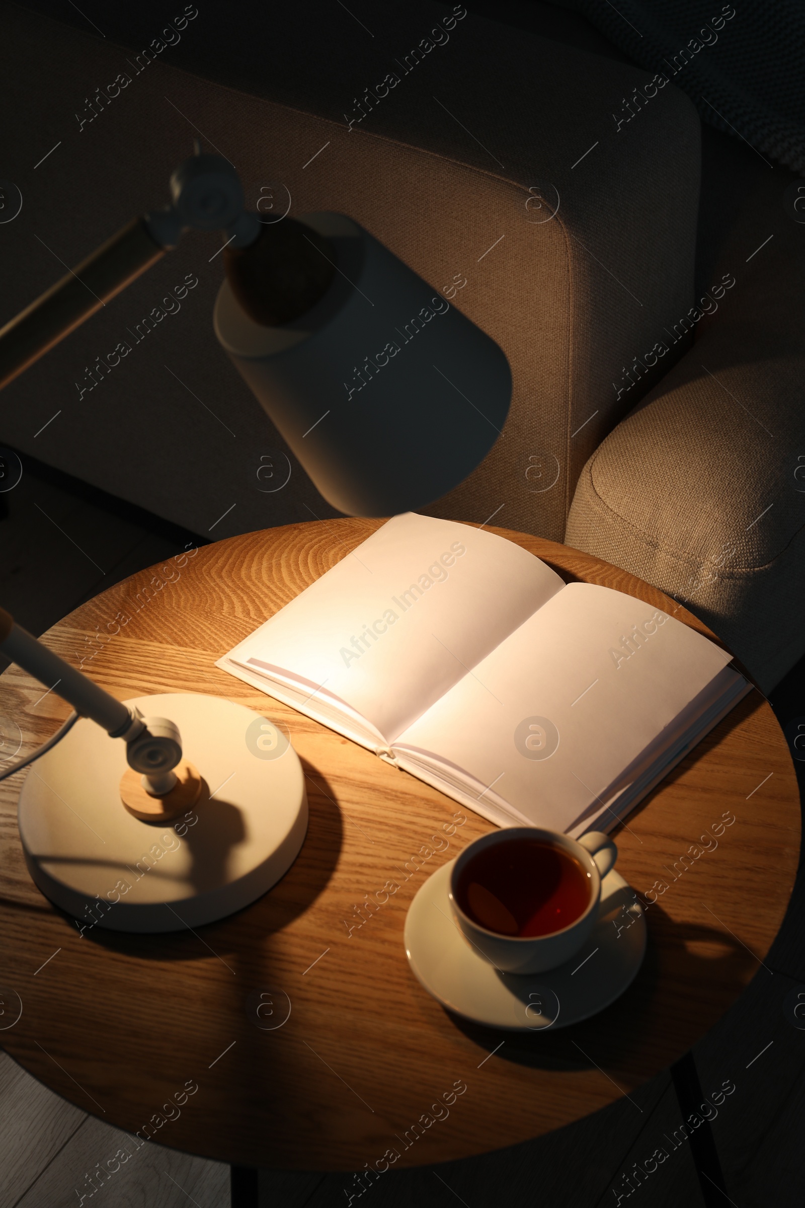 Photo of Stylish lamp, book and cup of tea on side table indoors