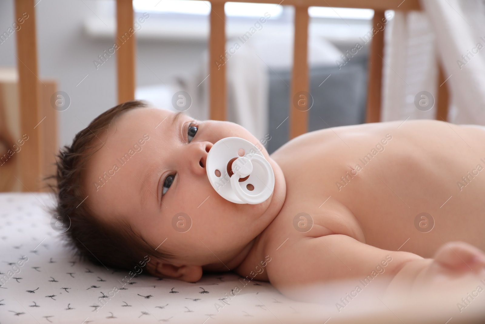 Photo of Cute little baby with pacifier lying in comfortable crib at home. Bedtime