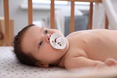 Photo of Cute little baby with pacifier lying in comfortable crib at home. Bedtime