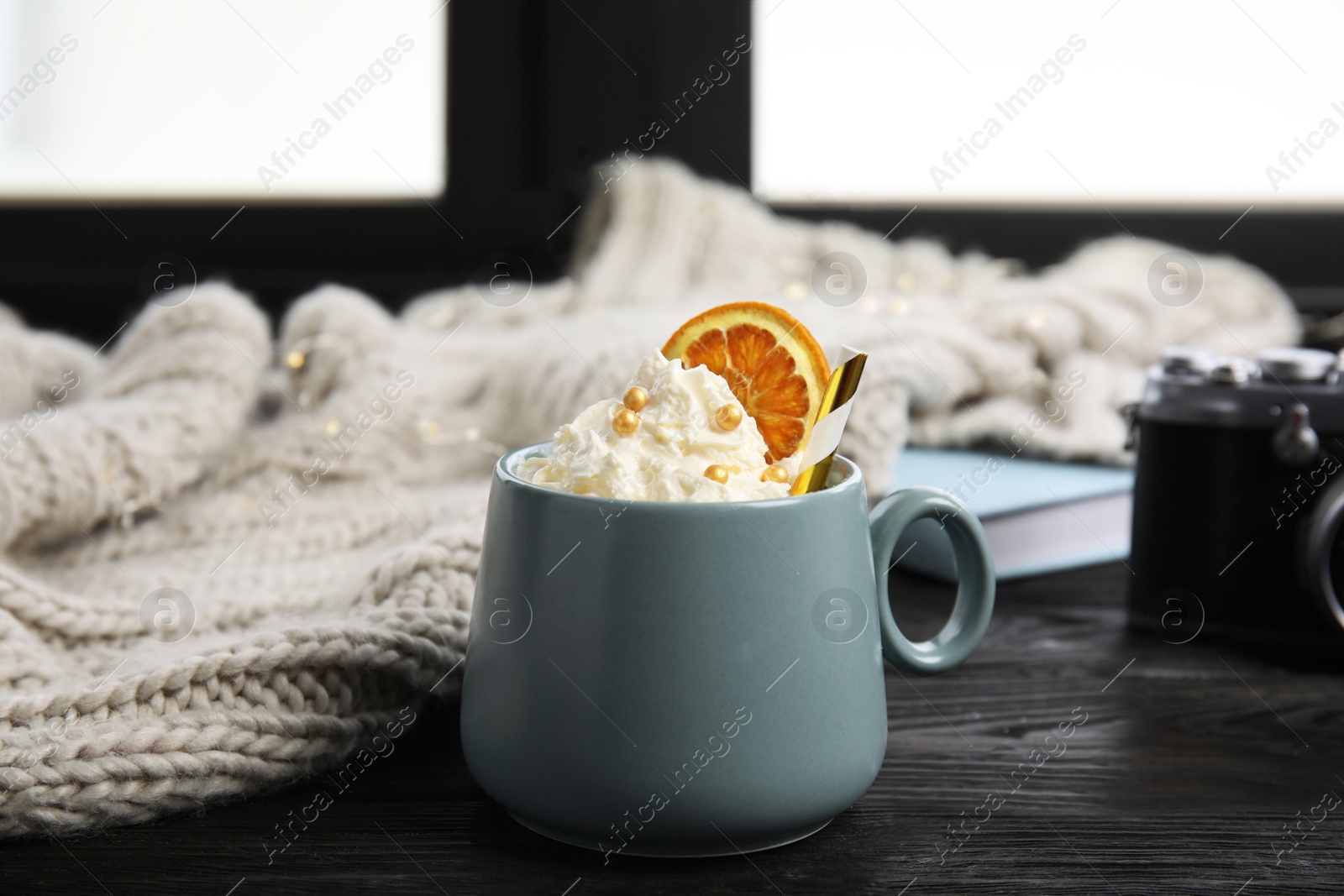 Photo of Cup of winter drink with whipped cream and knitted scarf on window sill