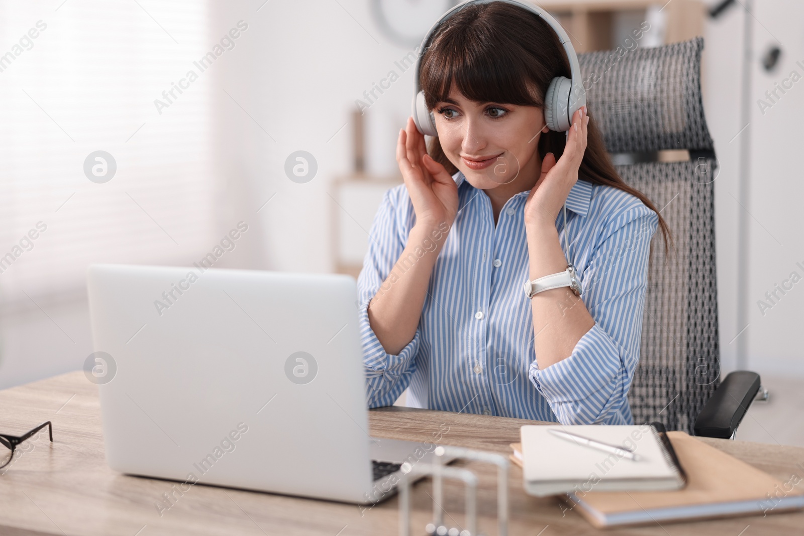 Photo of Woman in headphones watching webinar at wooden table in office