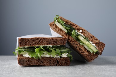 Tasty sandwiches with cream cheese, cucumber and greens on light grey table